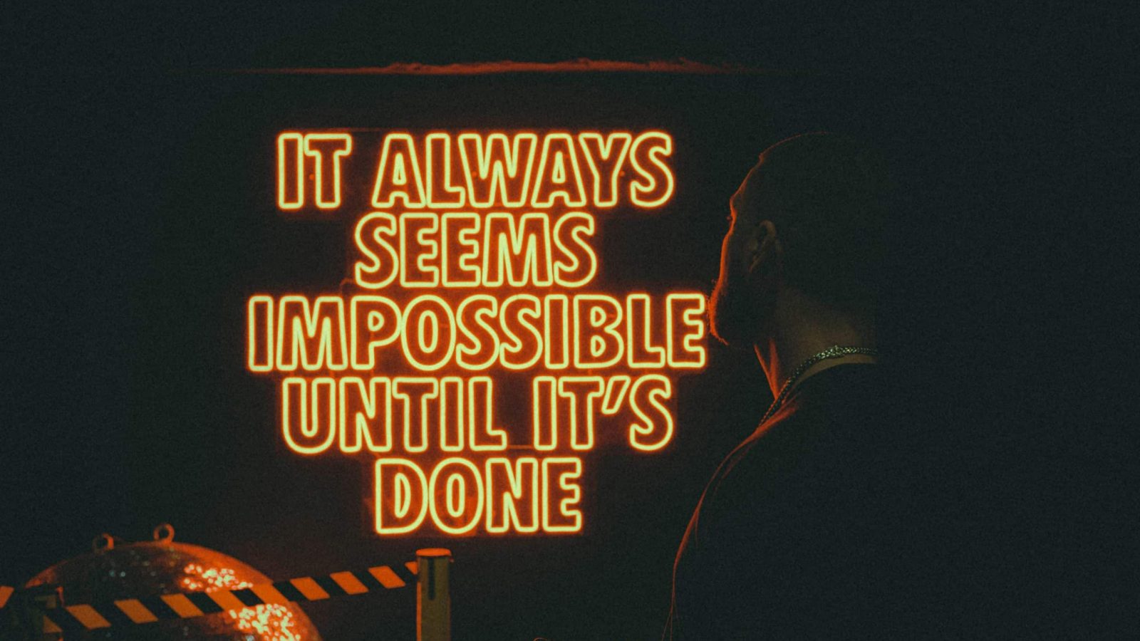 Ein Mann, der auf eine Leuchtreklame blickt - "It always seems impossible until ti's done"